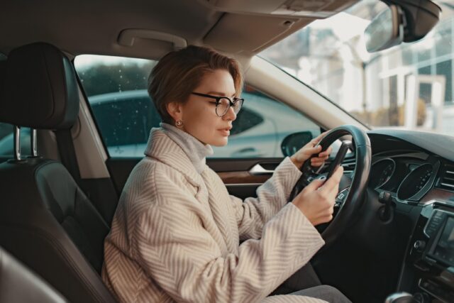 Frau im Auto hinter dem Steuer mit Handy in der Hand.